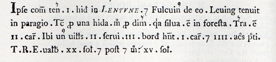 A close-up of a medieval Latin manuscript with black printed text and abbreviations, including references to land, holdings, and numbers, on a white background.