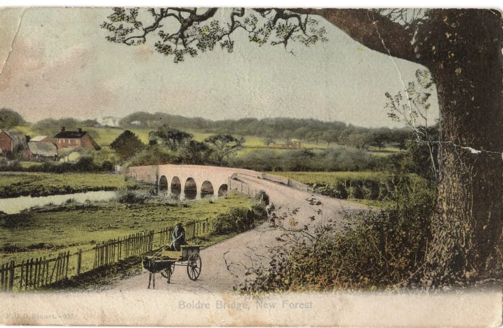 Vintage postcard of a rural scene showing Boldre Bridge in New Forest, with a person pushing a trolley along a winding road, fields, trees, and cottages in the background.