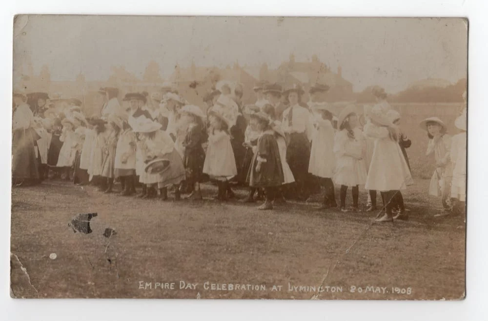 A vintage photo shows a large group of women and children in early 1900s clothing standing outdoors at the Empire Day Celebration at Lymington, dated 20 May 1908.
