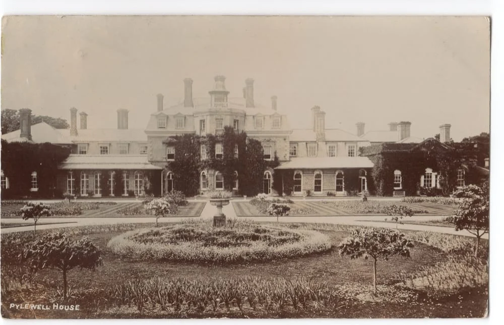 Sepia-toned photo of Pylewell House, a large historic mansion with many chimneys, ivy-covered walls, and formal gardens featuring circular flower beds and pathways in the foreground.