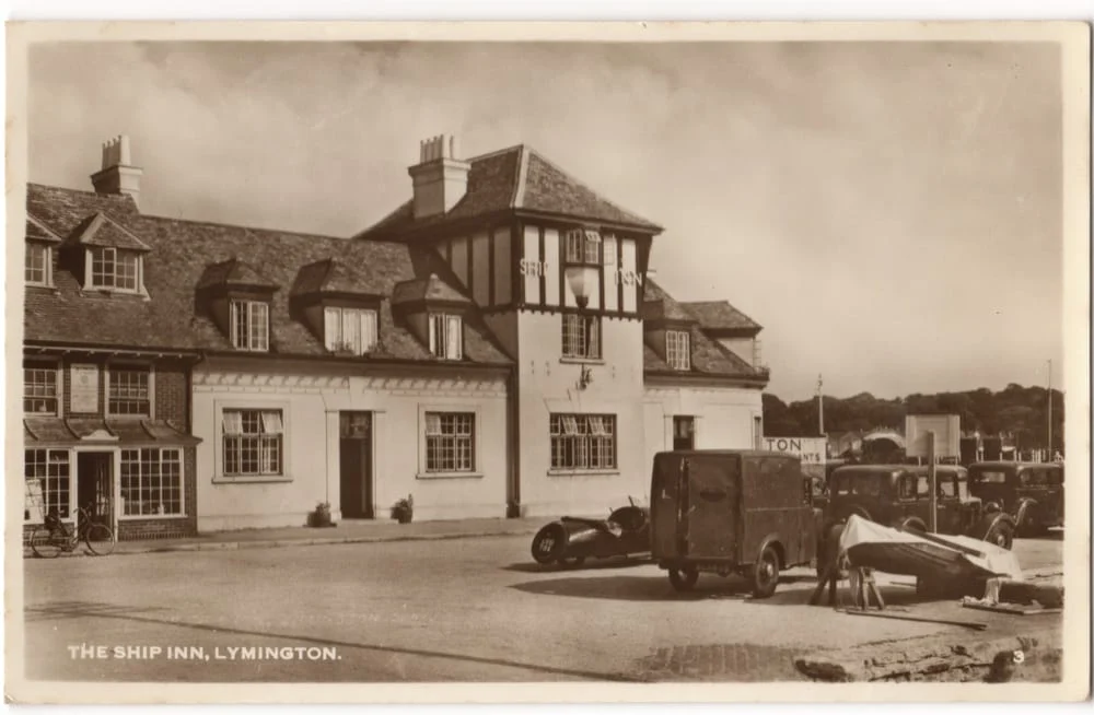 A vintage black-and-white photo of The Ship Inn in Lymington, showing a large building with multiple chimneys and cars parked outside, suggesting an early 20th-century scene.
